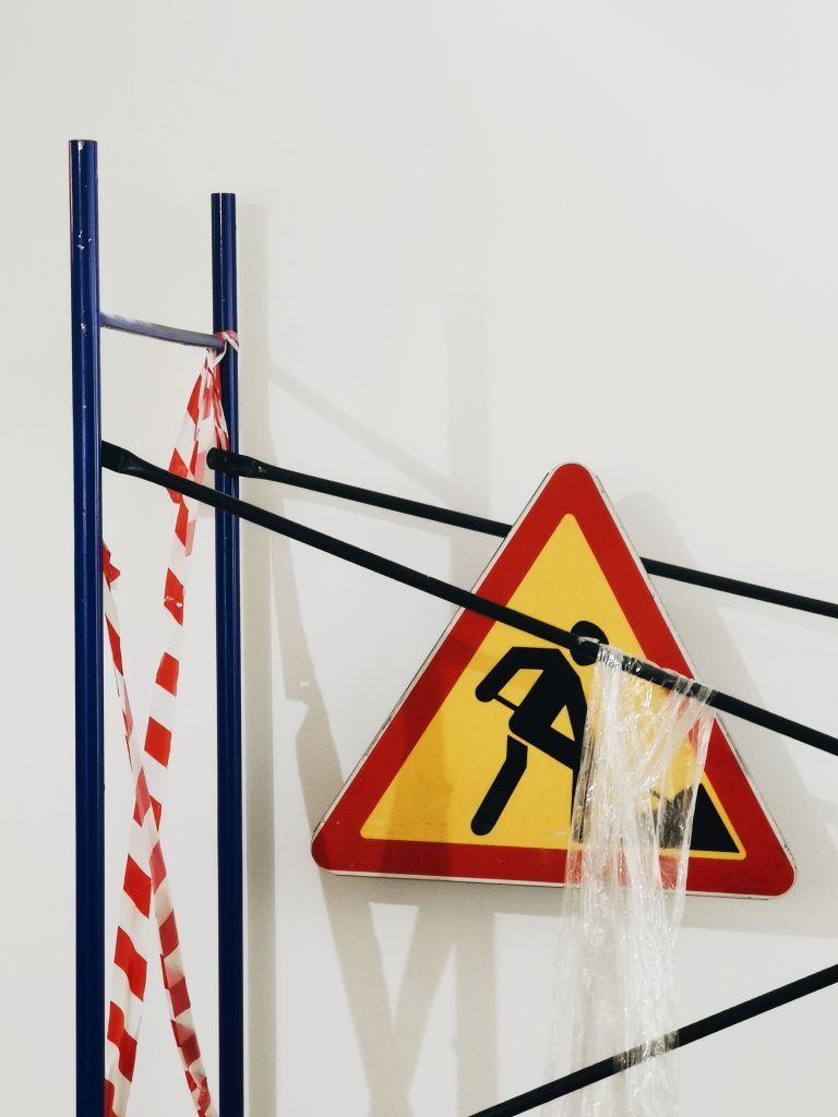 A triangular caution sign hanging on a metal structure with tape indoors, symbolizing safety.